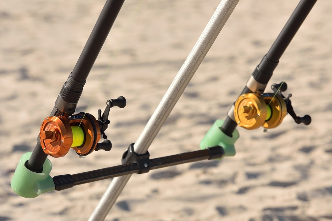 dwa kołowrotki do surfcastingu na tle morskiego piasku