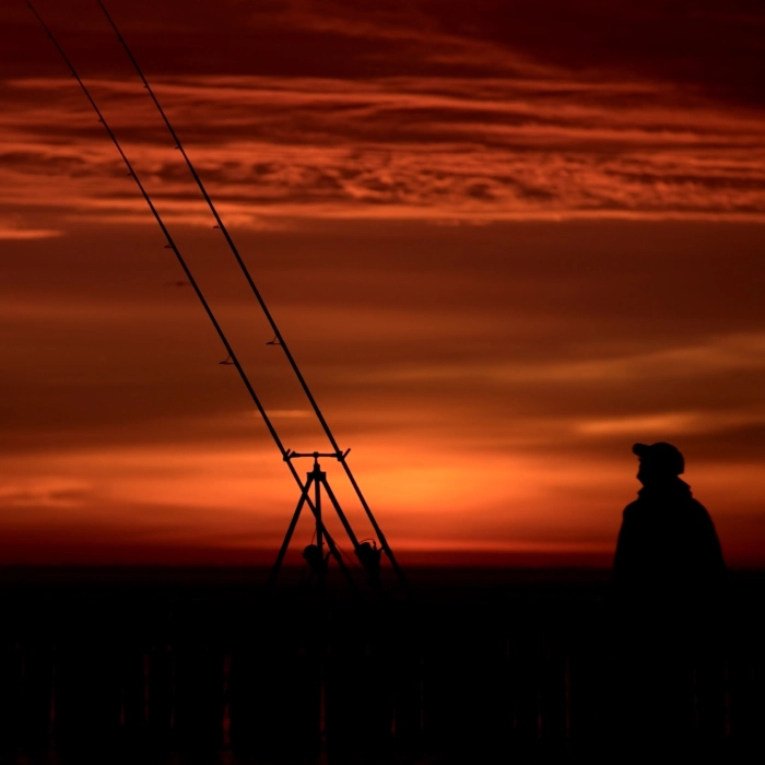 Sylwetka wędkarza o brzasku na tle wędek morskich