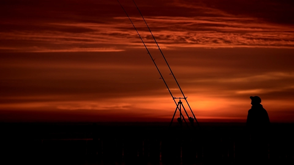 Zdjęcie wędkarza morskiego na tle wschodu słońca